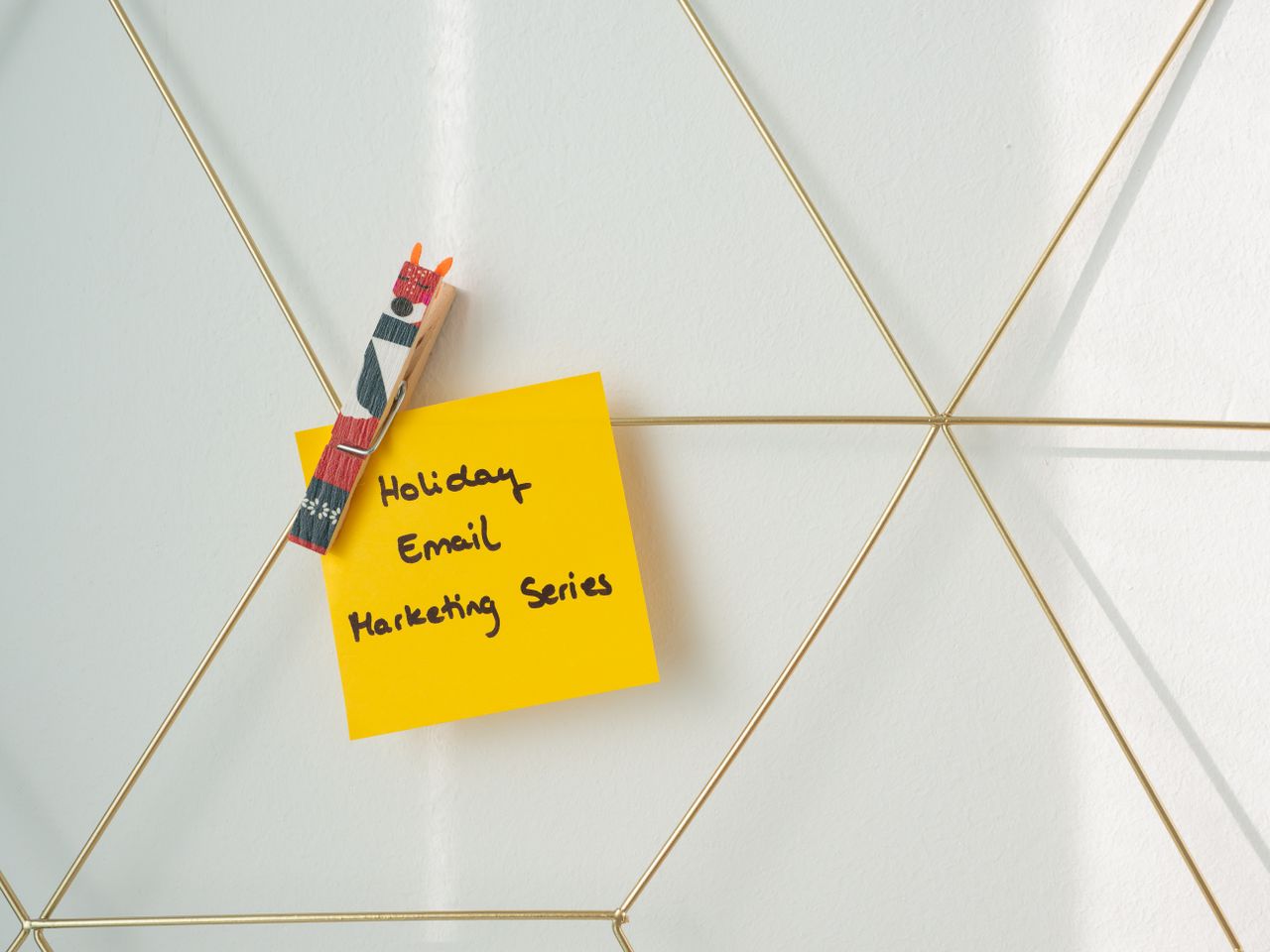 Post-it giallo brillante con un messaggio di email marketing per le festività, fissato a una parete a griglia.